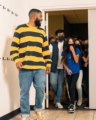 Khalid walking into a room wearing a black and yellow striped shirt.