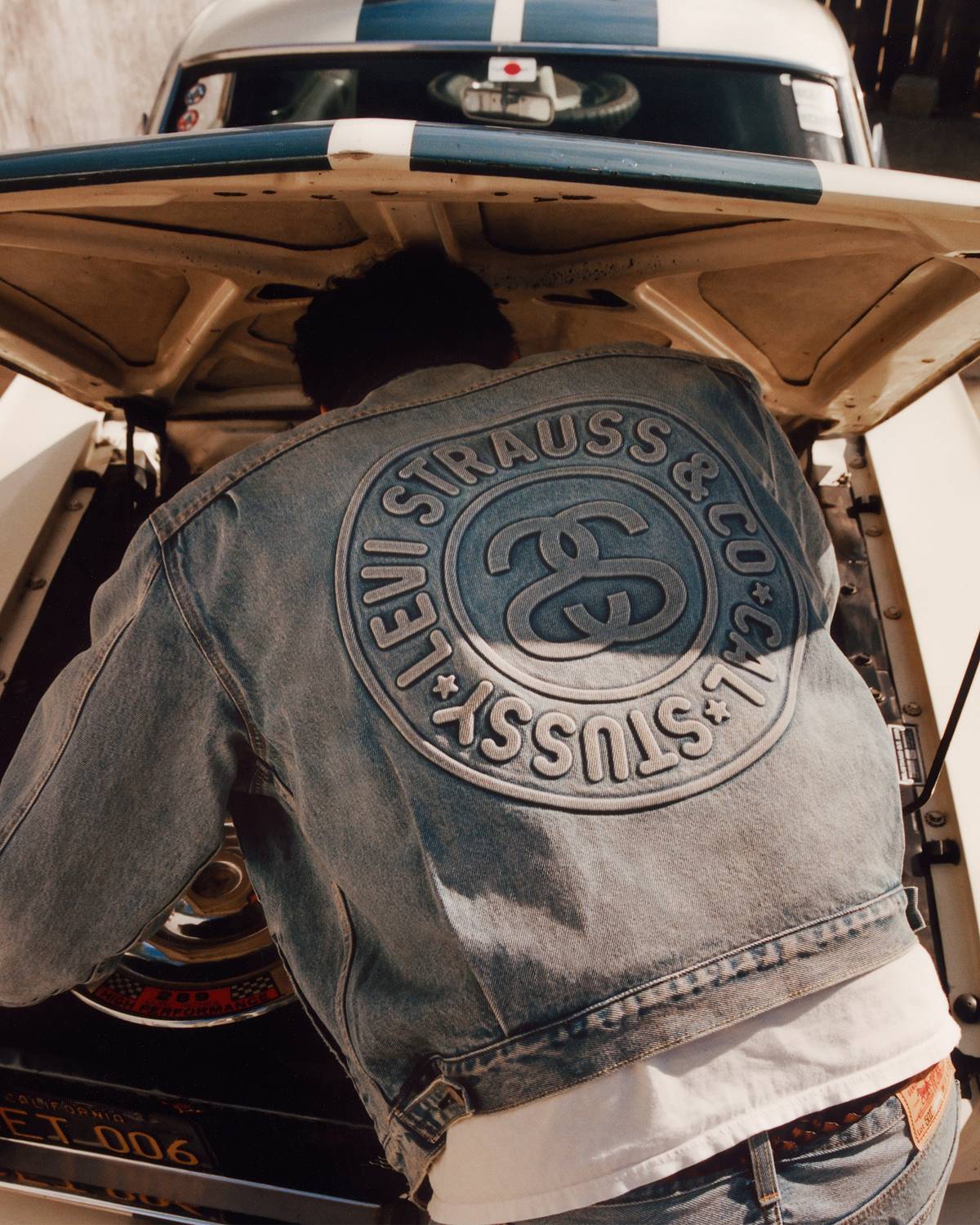 A person reaching into the trunk of a car while wearing the Stüssy & Levi's® collaboration medium-wash trucker jacket.