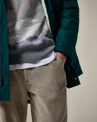 Closeup of dark green parka, mountain inspired woven sweater and grooved beige pants 2022_fall_outfits_for_men