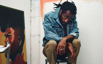 Portrait of Joonbug sitting in his studio next to a painting.