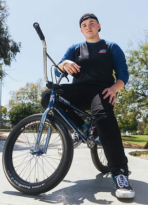 Hannah sitting on a bmx bike wearing a dark long sleeve, jeans, and a backwards cap
