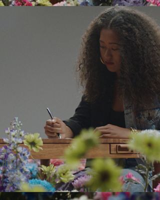 Naomi Osaka writing on a wooden table, surrounded by flowers.