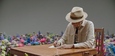 Carlos Montes sitting at a desk writing in a field of flowers