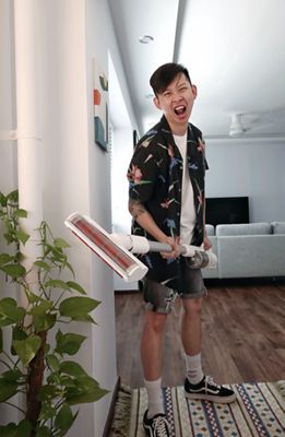 Photo of Mark Chan brandishing a portable vacuum. He is wearing a tropical-print Cubano shirt over a white tee with cut-off denim shorts and white socks with black Vans.
