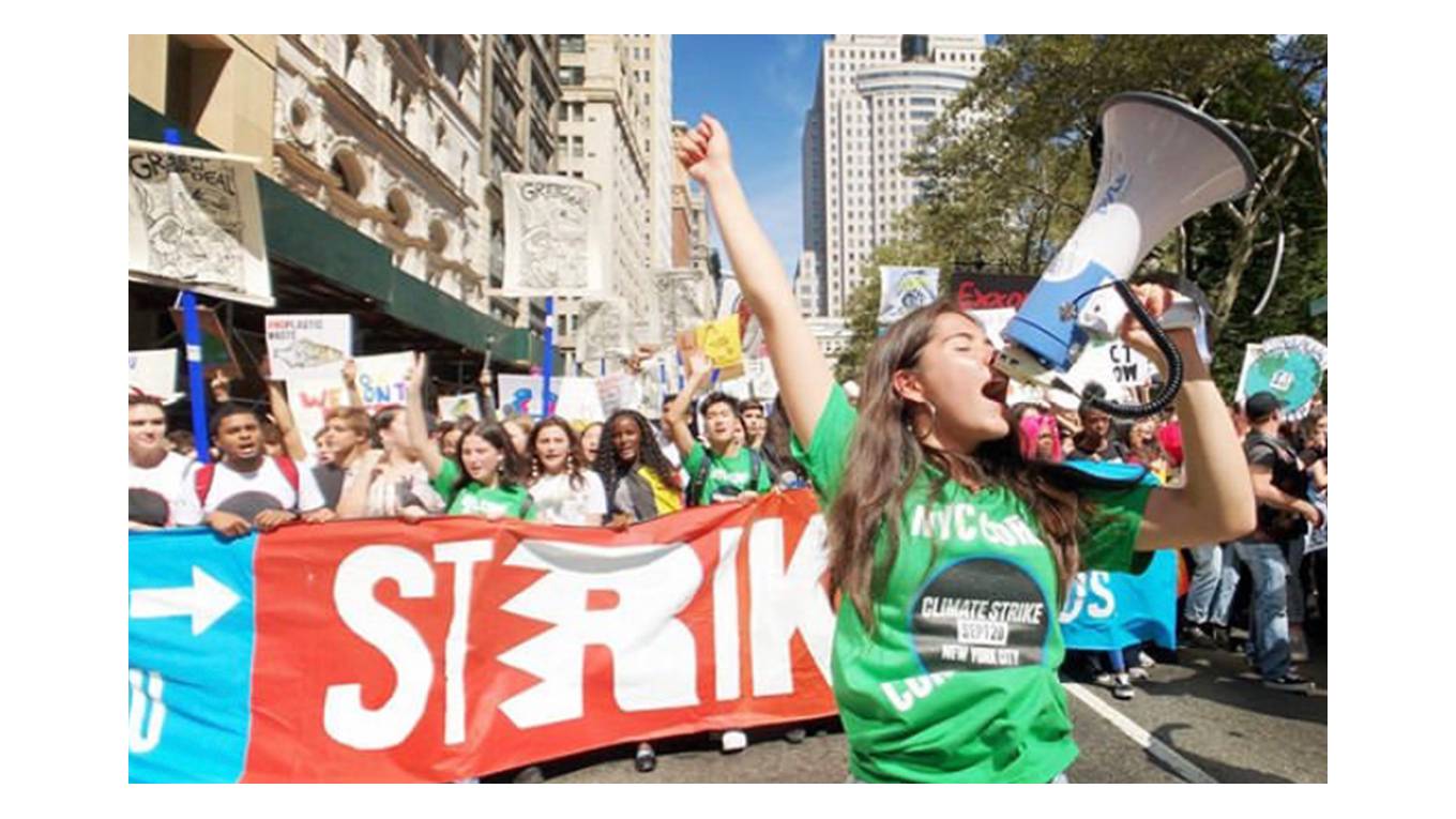 Photo of Xiye Bastida leading a protest. She is speaking into a megaphone and is wearing a green shirt.