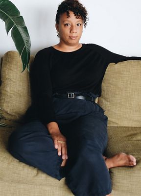Photo of Solange Parris sitting on a couch. She is wearing all black.