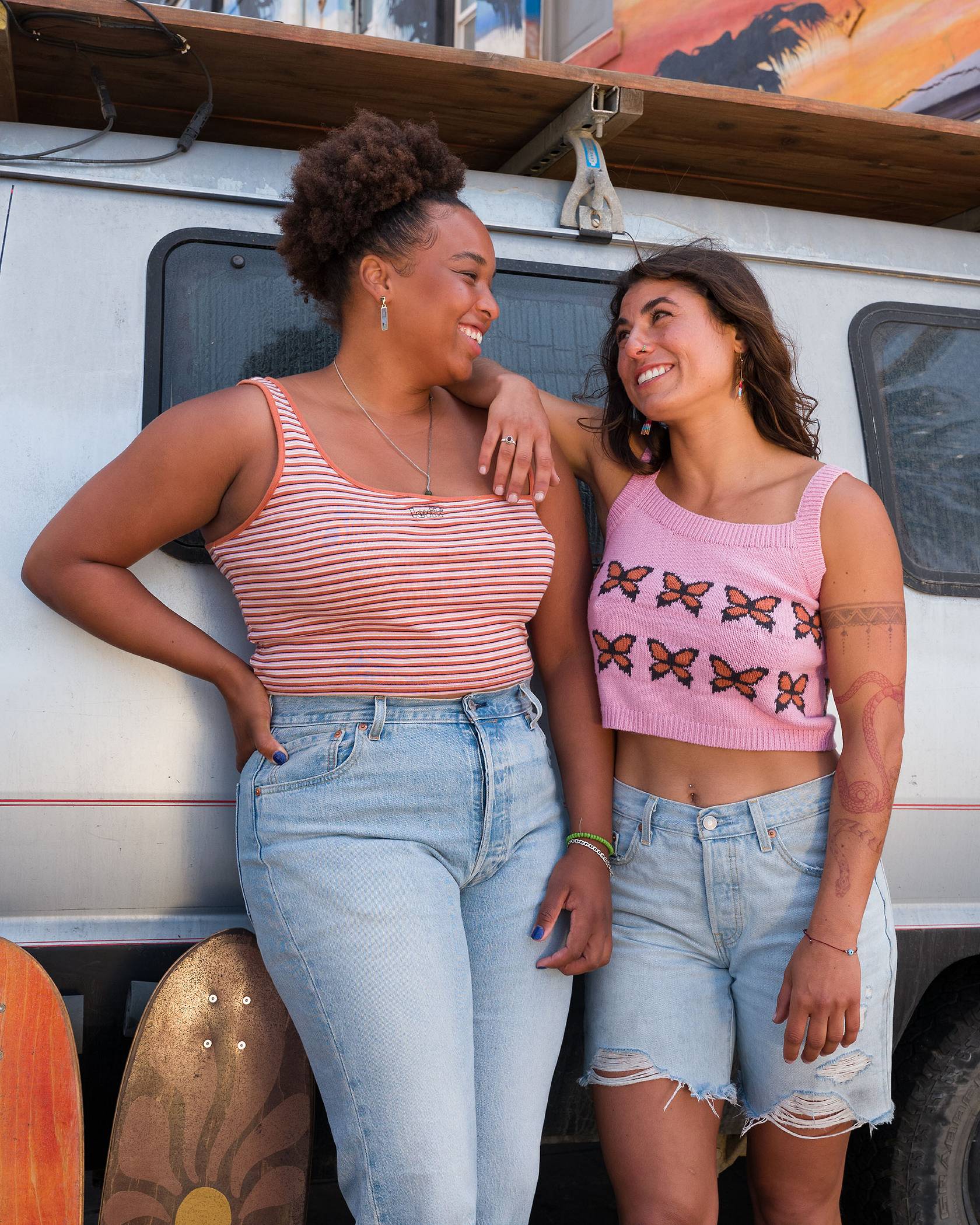 Two woman wearing summer fashion/4th of July outfits/summer denim - one is in a one shoulder tank and jeans, the other a woven butterfly tank and cutoff shorts