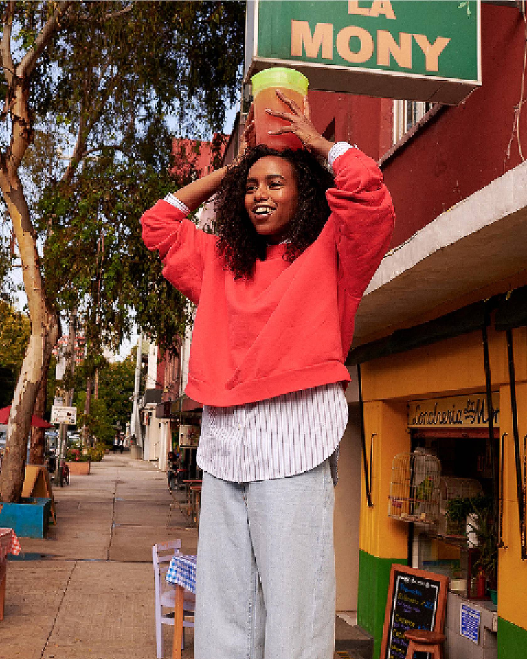 Woman wearing an orange sweatshirt and holding a pitcher of liquid over her head.