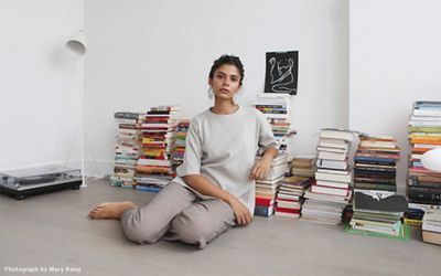 Image of Tasnim Ahmed sitting on the floor with stacks of books behind her.