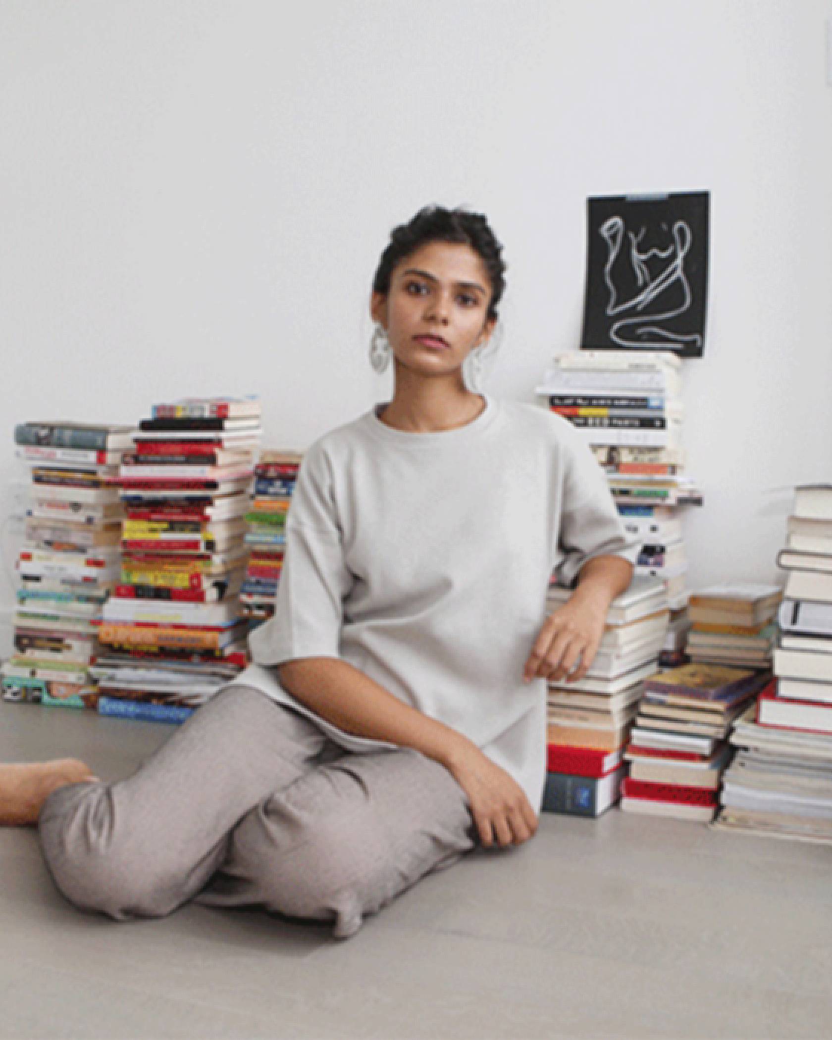 Image of Tasnim Ahmed sitting on the floor with stacks of books behind her.