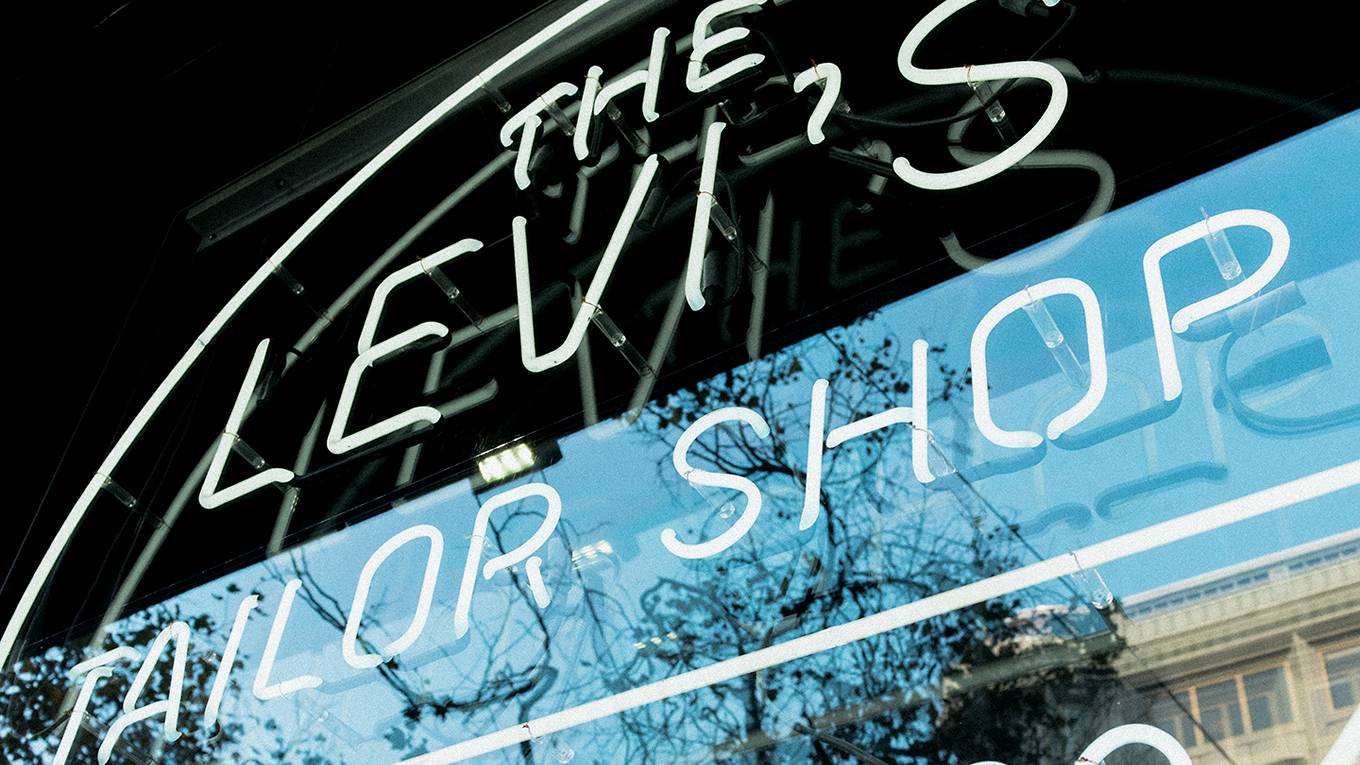 The window of a Levi's tailor shop with an electric sign saying, "The Levi's Tailor Shop"