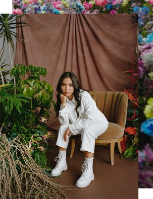 A portrait of Xiye Bastida sitting down, wearing a white Levi's jacket and white Levi's jeans