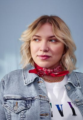 Portrait of Sabine Sadnik wearing a light wash blue denim trucker jacket, red handkerchief, and white Levi's® logo tee shirt, looking away from the camera.