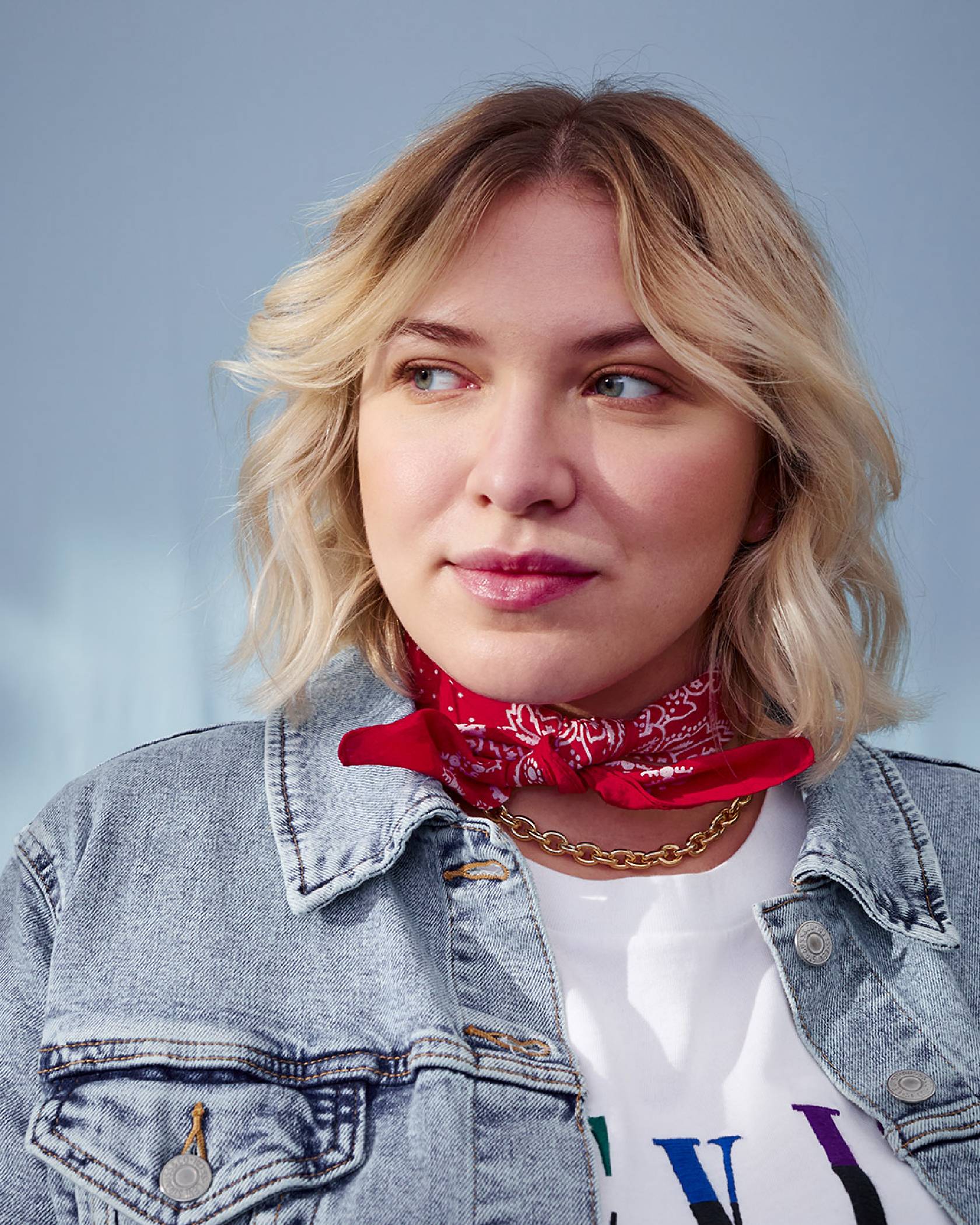 Portrait of Sabine Sadnik wearing a light wash blue denim trucker jacket, red handkerchief, and white Levi's® logo tee shirt, looking away from the camera.