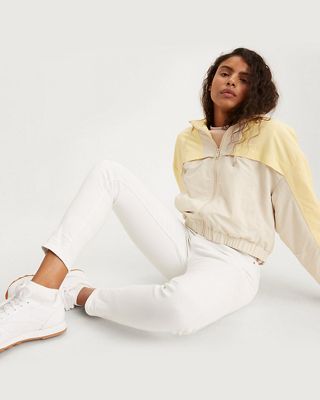 Model wearing white jeans and yellow and beige zip up jacket